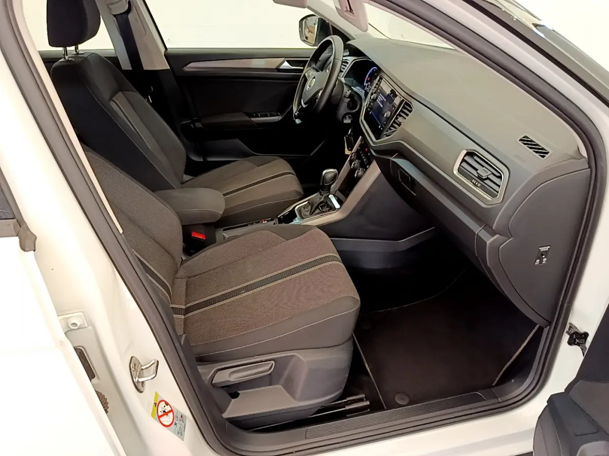 Intérieur avant droit d'un Volkswagen T-Roc blanc 2021, sièges tissu gris et tableau de bord moderne avec écran tactile.
