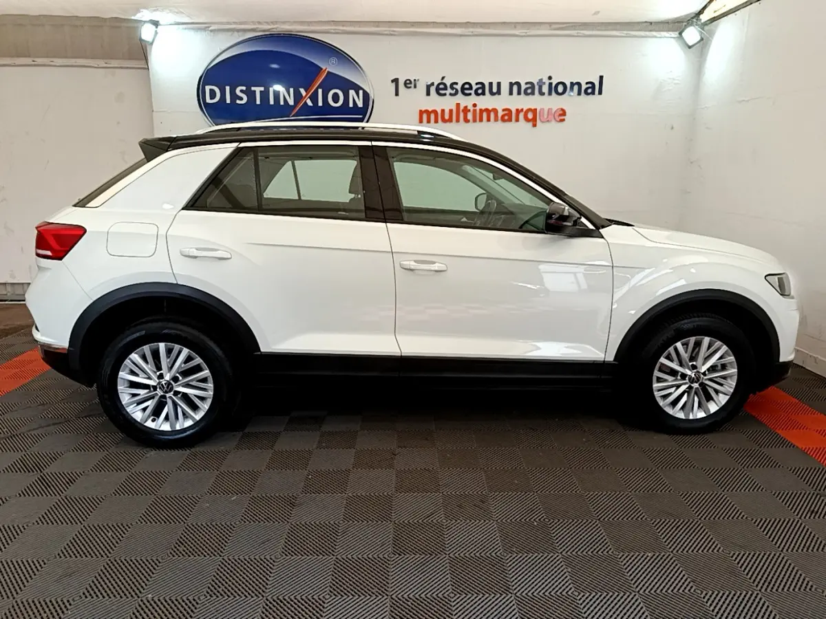 Profil droit d'un Volkswagen T-Roc blanc 2021 avec jantes alliage et toit noir dans un showroom intérieur.