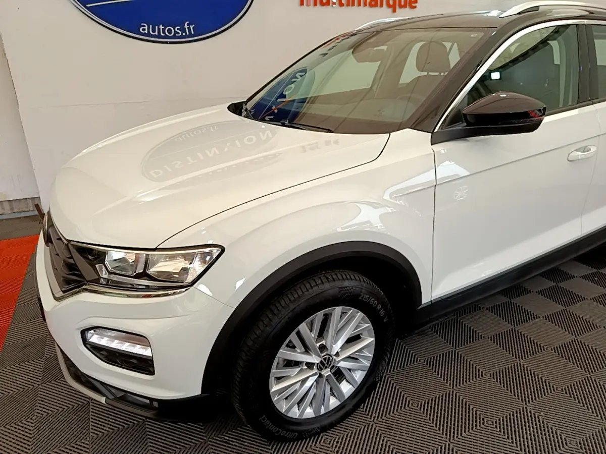 Vue 3/4 avant droit d'un Volkswagen T-Roc blanc avec jantes alliage et rétroviseurs noirs brillants.