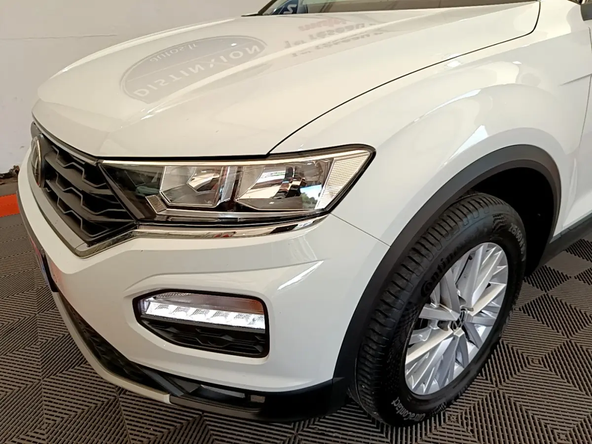 Vue 3/4 avant droit d'un Volkswagen T-Roc blanc mettant en valeur ses phares et jantes alliage.
