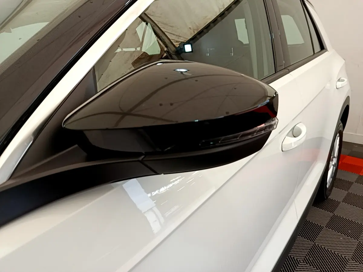 Rétroviseur noir côté conducteur en gros plan sur Volkswagen T-Roc blanc, vue latérale droite du véhicule.