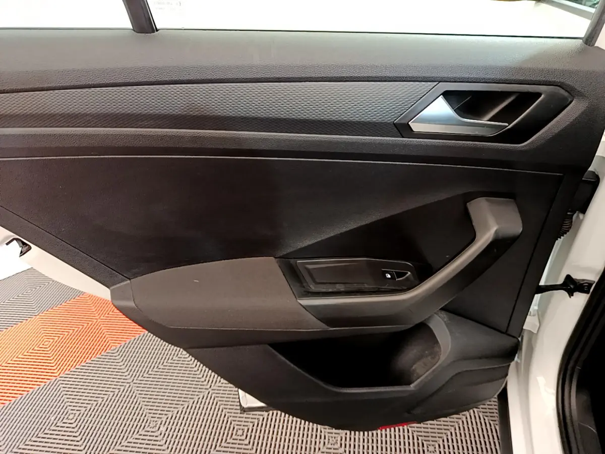 Vue rapprochée de la porte avant droite noire du Volkswagen T-Roc blanc, avec poignée et commande de vitre électrique.
