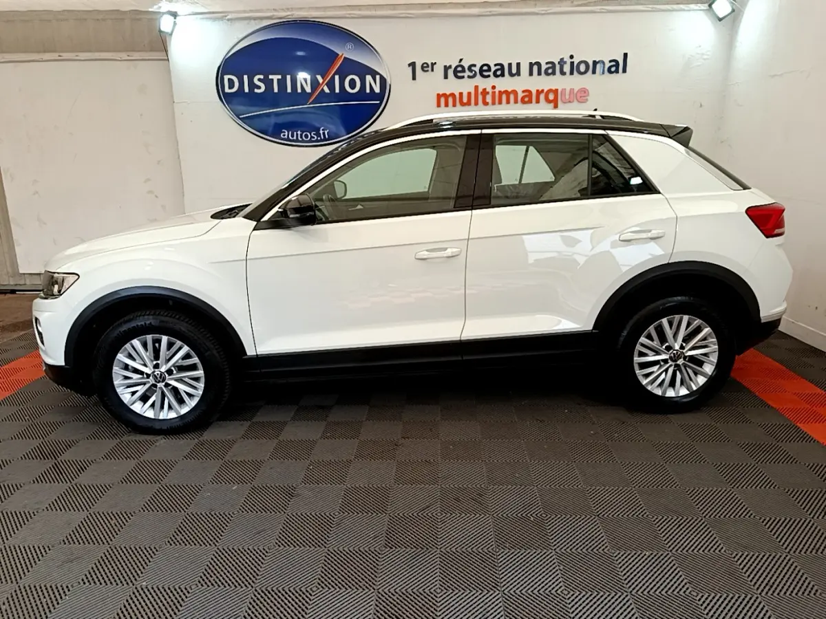 Profil côté gauche d'un Volkswagen T-Roc blanc 2021 avec jantes alliage et toit noir en showroom.