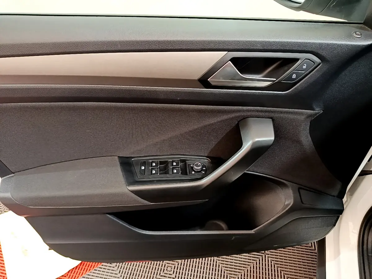 Vue rapprochée de la porte côté conducteur du Volkswagen T-Roc blanc, avec commandes électriques et poignée noire.