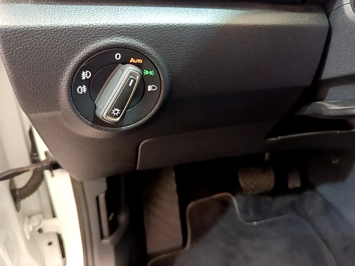 Gros plan sur le bouton de commande des phares dans l’habitacle noir du Volkswagen T-Roc blanc côté conducteur.