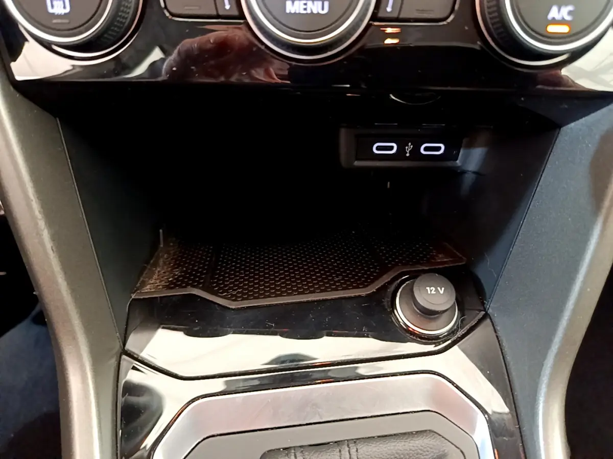 Vue rapprochée de la console centrale noire du Volkswagen T-Roc blanc, avec prise 12V et ports USB visibles.