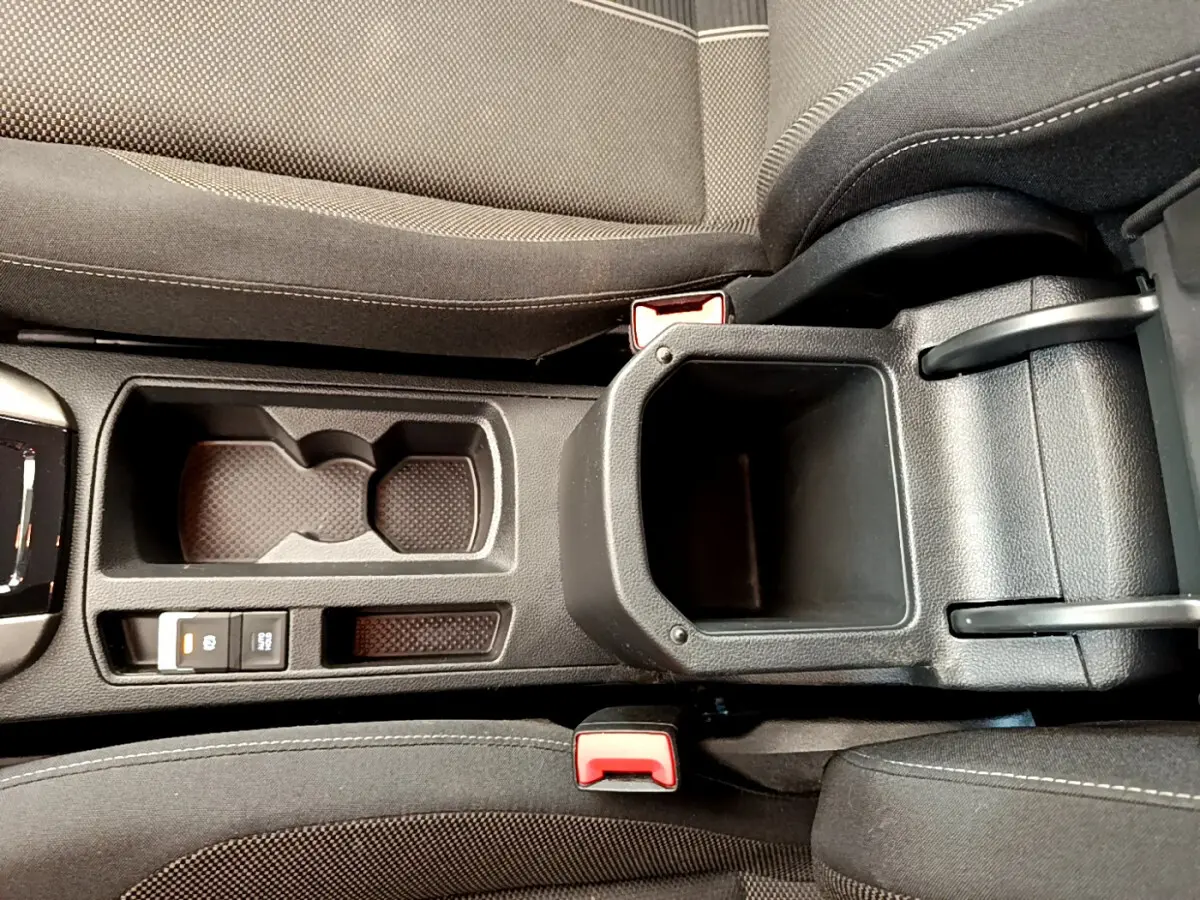 Vue plongeante sur la console centrale noire du Volkswagen T-Roc blanc, avec porte-gobelets et frein à main électrique.
