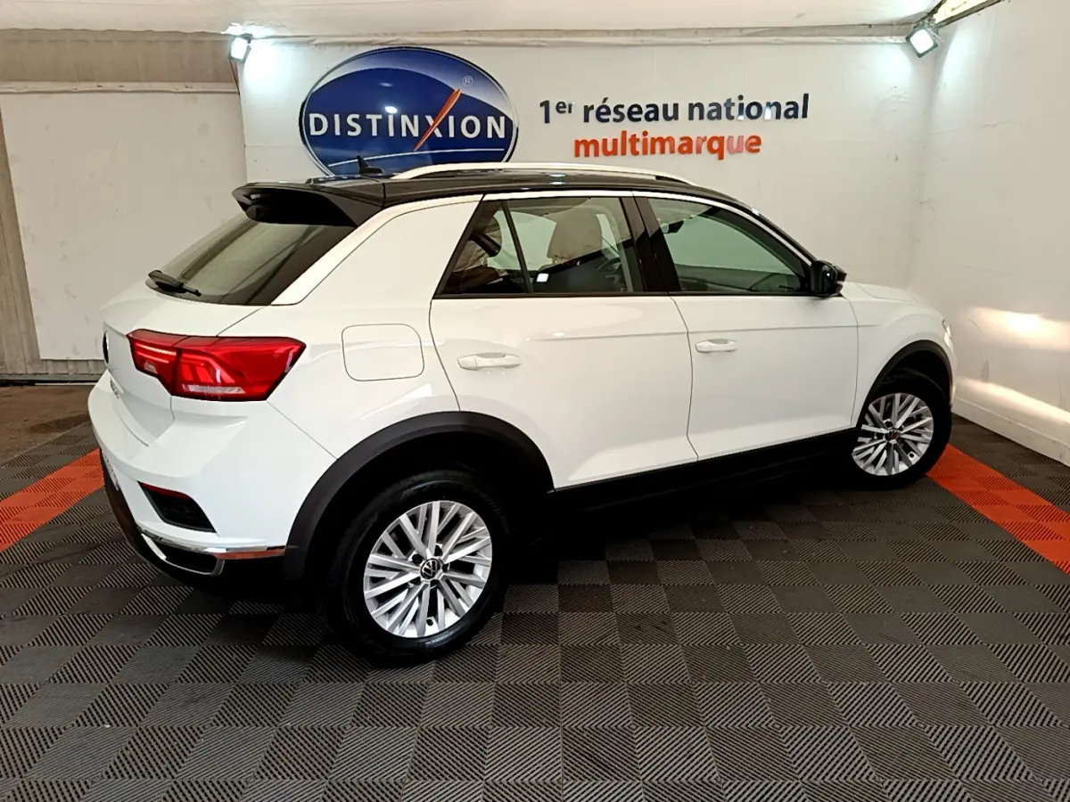 Volkswagen T-Roc blanc en 3/4 arrière droit, toit noir contrasté et jantes alliage dans showroom intérieur.