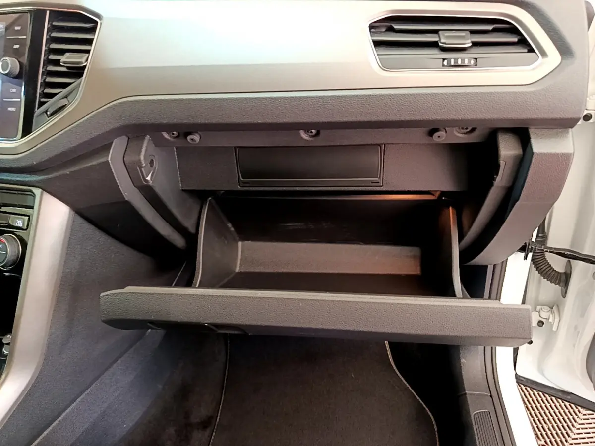 Gros plan sur la boîte à gants ouverte côté passager du Volkswagen T-Roc blanc, tableau de bord moderne visible.