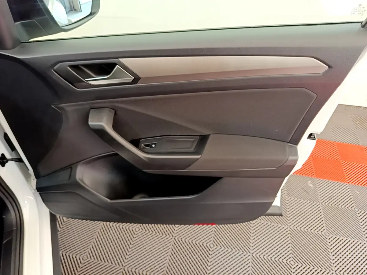 Porte côté conducteur ouverte d’un Volkswagen T-Roc blanc, intérieur noir avec poignée et commande de vitre intégrée.