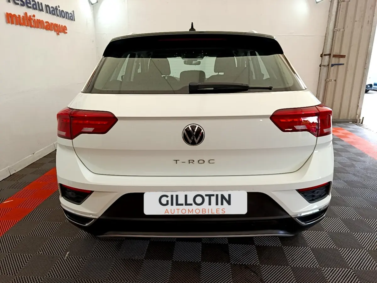 Vue arrière d'un Volkswagen T-Roc blanc avec feux arrière rouges et toit noir dans un garage.