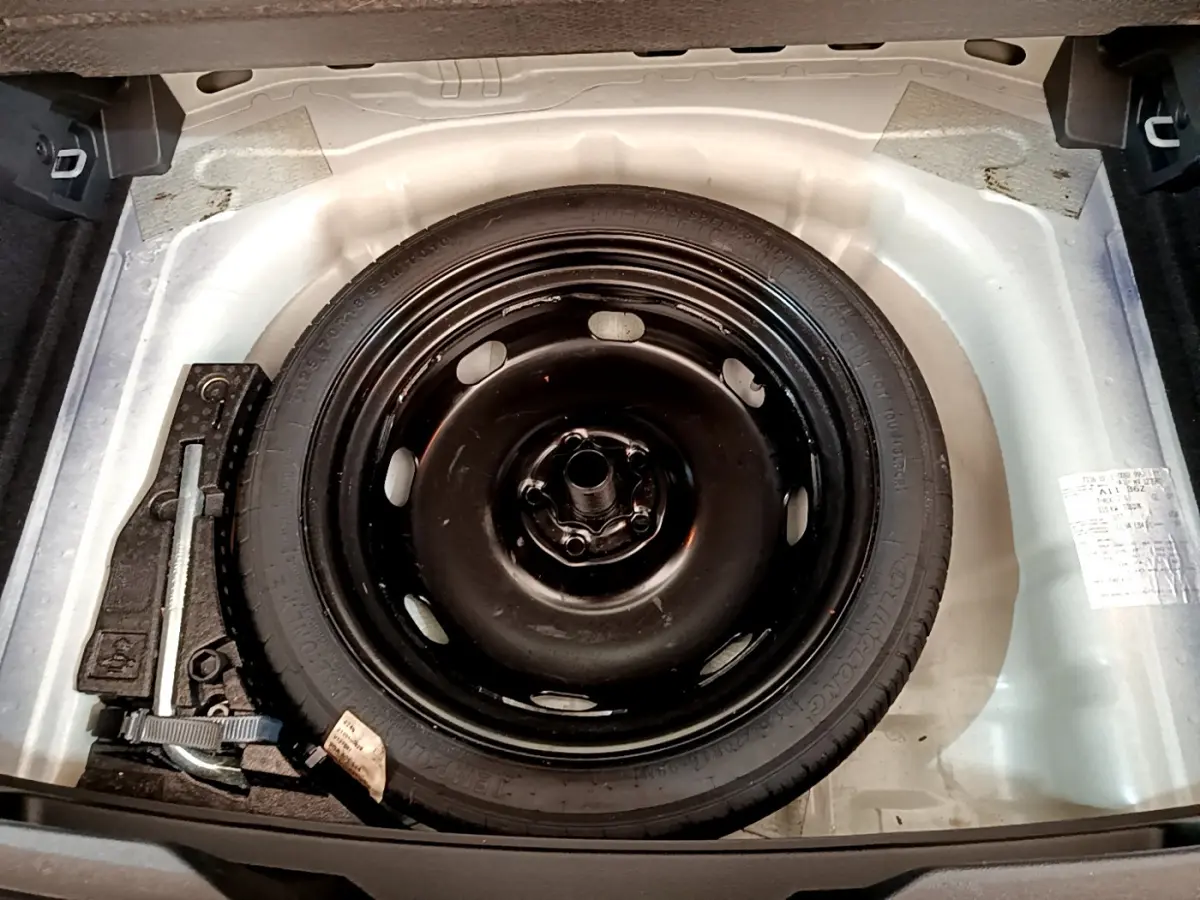 Roue de secours galette noire dans le coffre blanc d'un Volkswagen T-Roc 2021, avec outils de changement visibles.