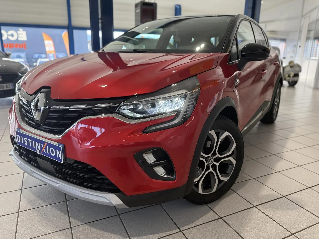 Vue 3/4 avant droit d’un Renault Captur rouge foncé avec jantes alliage et calandre chromée en showroom.