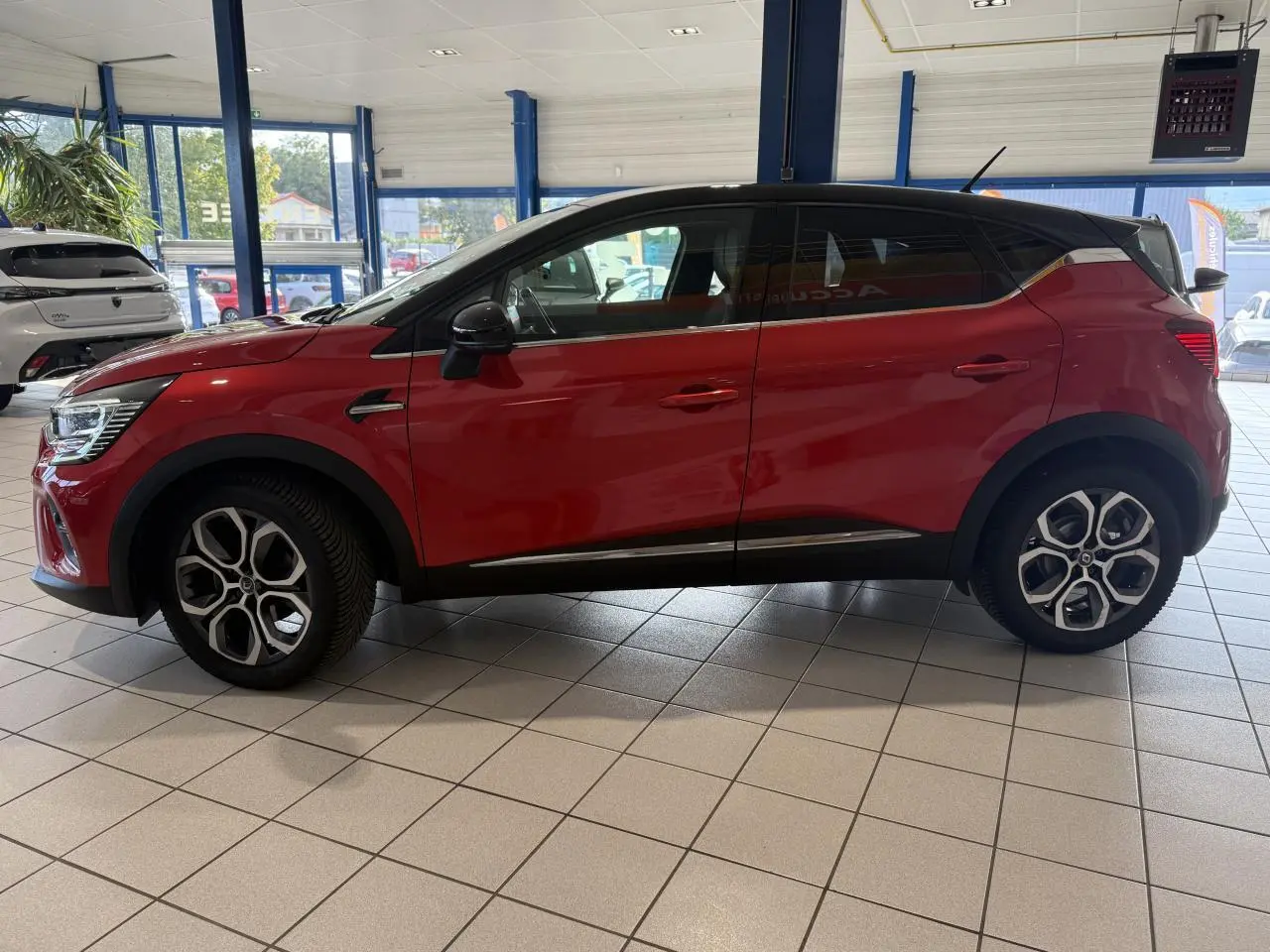 Profil côté gauche d'un Renault Captur 2020 rouge foncé avec jantes alliage et toit noir en showroom.