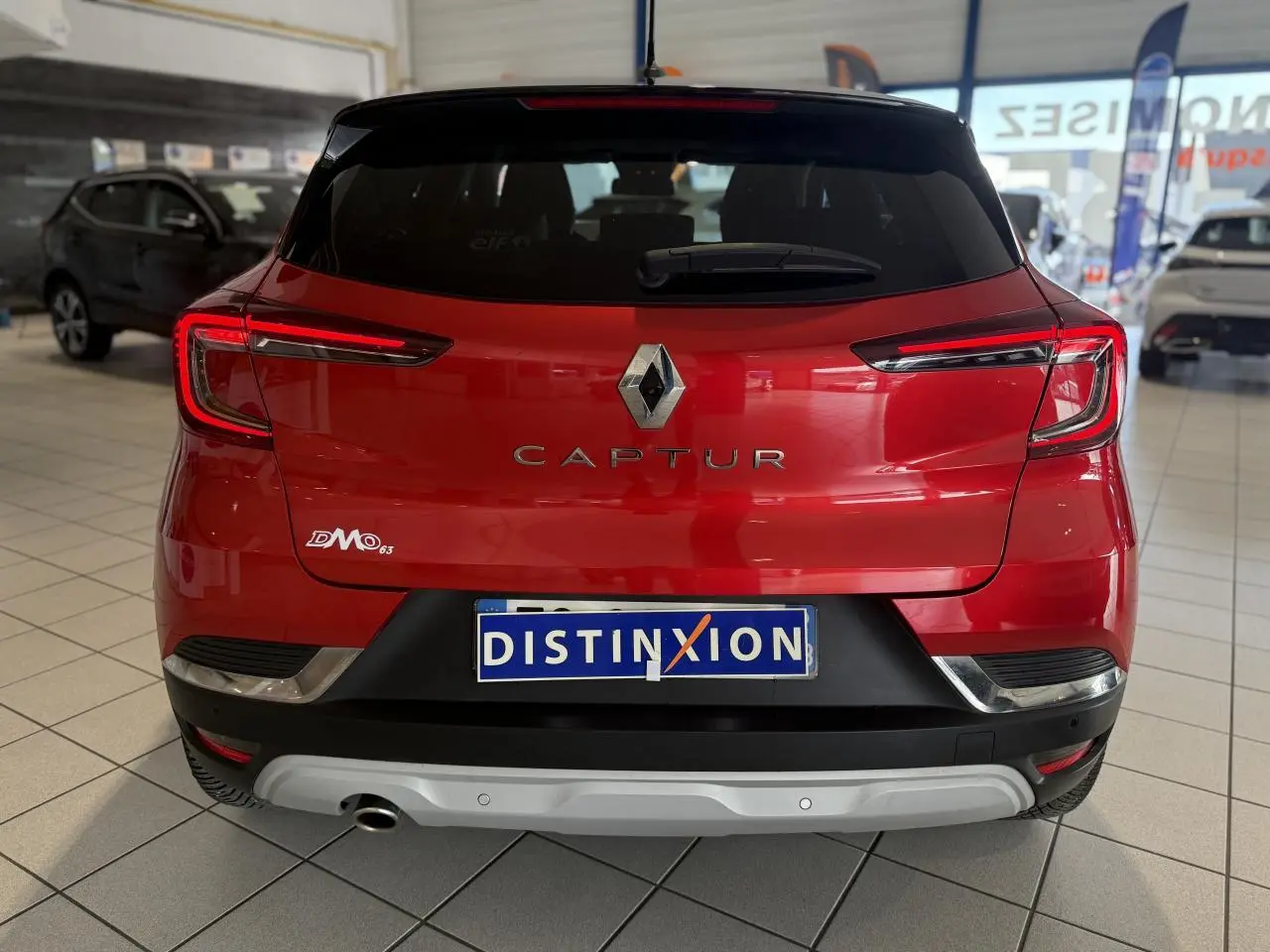 Vue arrière d'un Renault Captur rouge foncé dans un showroom, avec logo et plaque Distinxion visibles.