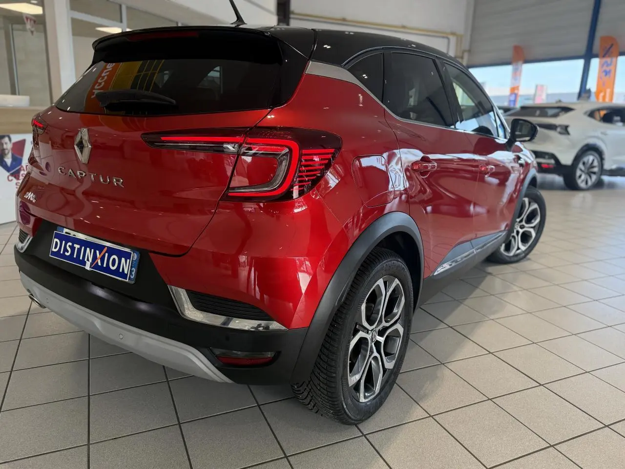 Vue 3/4 arrière droite d'un Renault Captur rouge foncé avec toit noir et jantes alliage en concession.