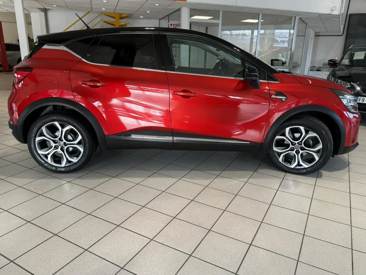 Profil droit du Renault Captur 2020 rouge foncé avec toit noir et jantes alliage en showroom.