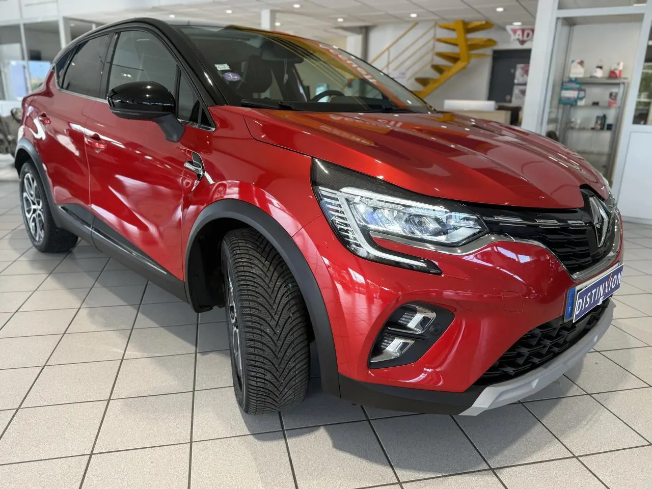 Renault Captur rouge foncé en 3/4 avant droit, avec phares allumés et jantes alliage visibles en showroom.