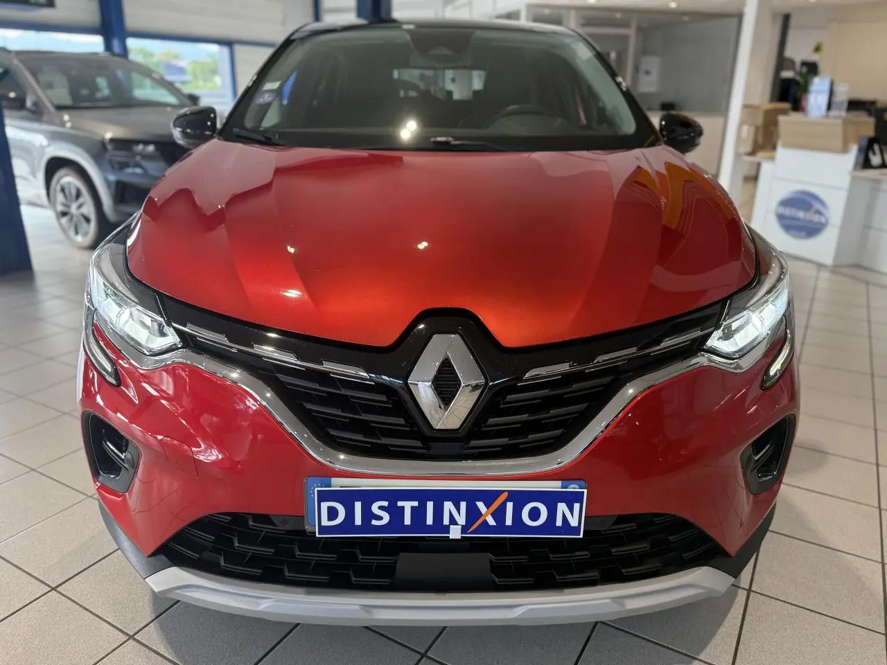 Vue frontale d'un Renault Captur rouge foncé avec calandre noire et logo Renault bien visible en showroom.