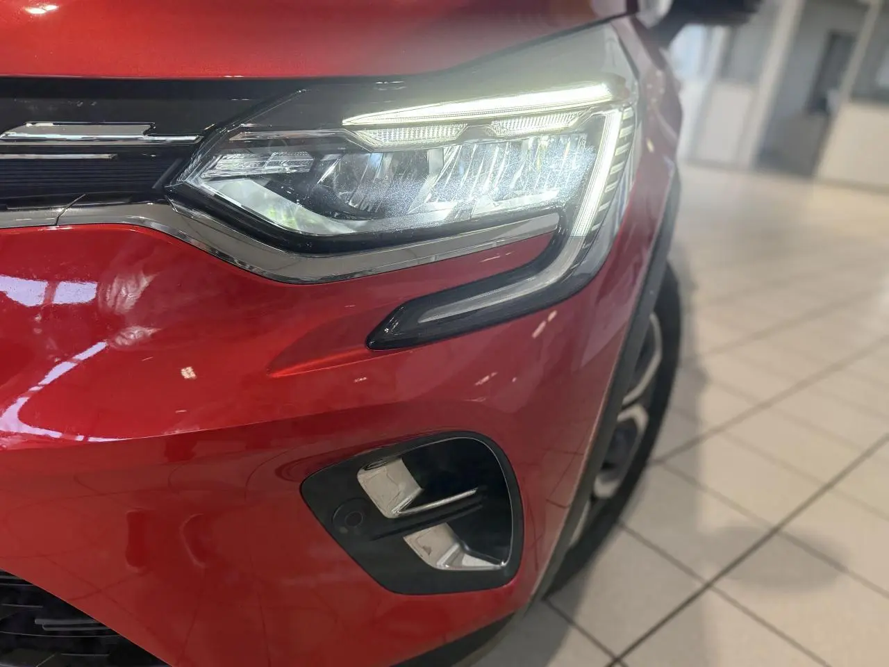 Gros plan sur le phare avant droit et le pare-chocs rouge foncé d'un Renault Captur 2020 en showroom.