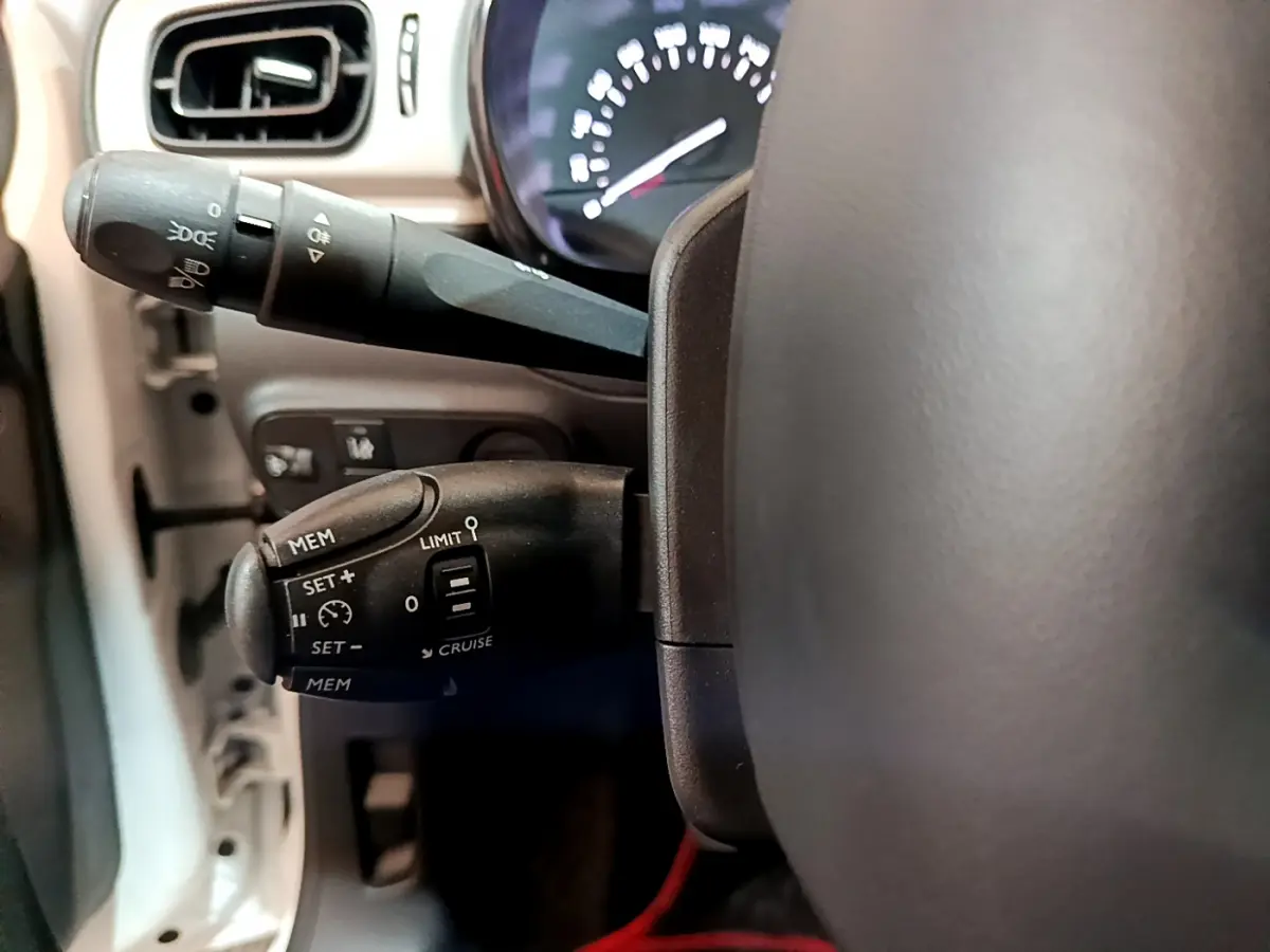 Gros plan sur les commandes du régulateur de vitesse et des phares à gauche du volant d'une Citroën C3 blanche de 2018.