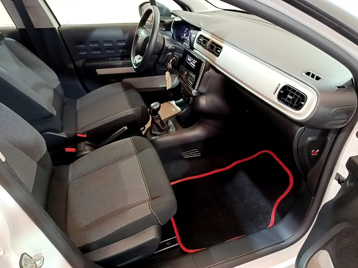 Vue intérieure côté passager avant de la Citroën C3 blanche, montrant sièges gris et tableau de bord avec console centrale.