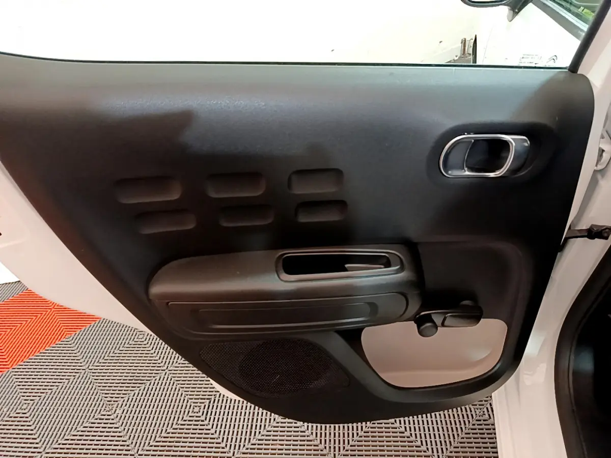 Vue intérieure de la porte avant gauche blanche d'une Citroën C3 2018 avec poignée chromée et commande de vitre manuelle.