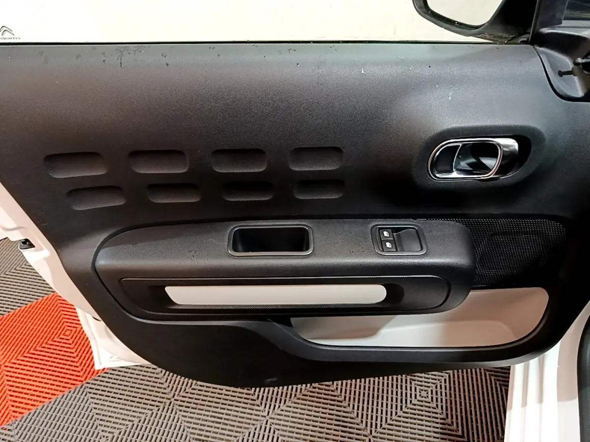 Vue rapprochée de la porte avant gauche blanche de la Citroën C3 2018 avec poignée intérieure chromée et boutons de fenêtre.