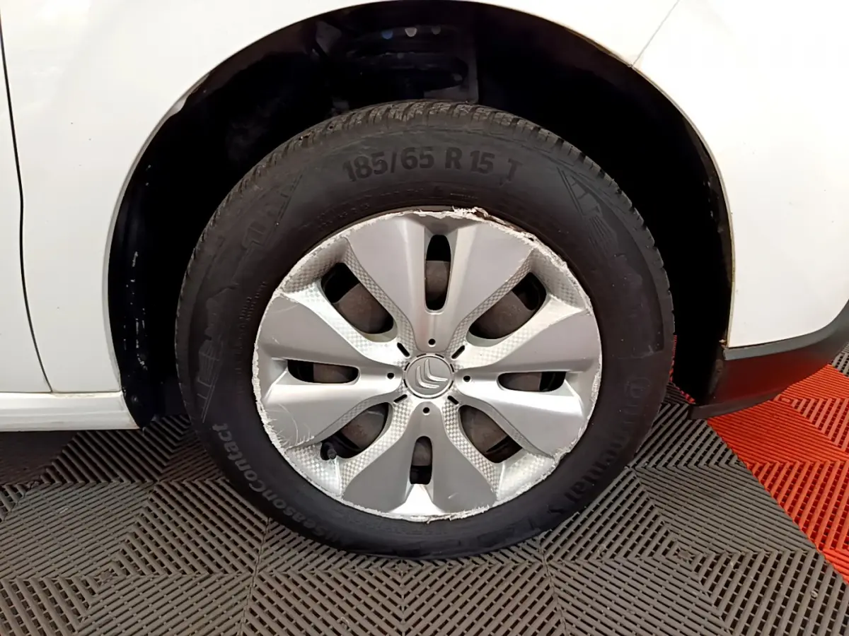Gros plan sur la roue avant droite d'une Citroën C3 blanche, jante avec enjoliveur endommagé visible.