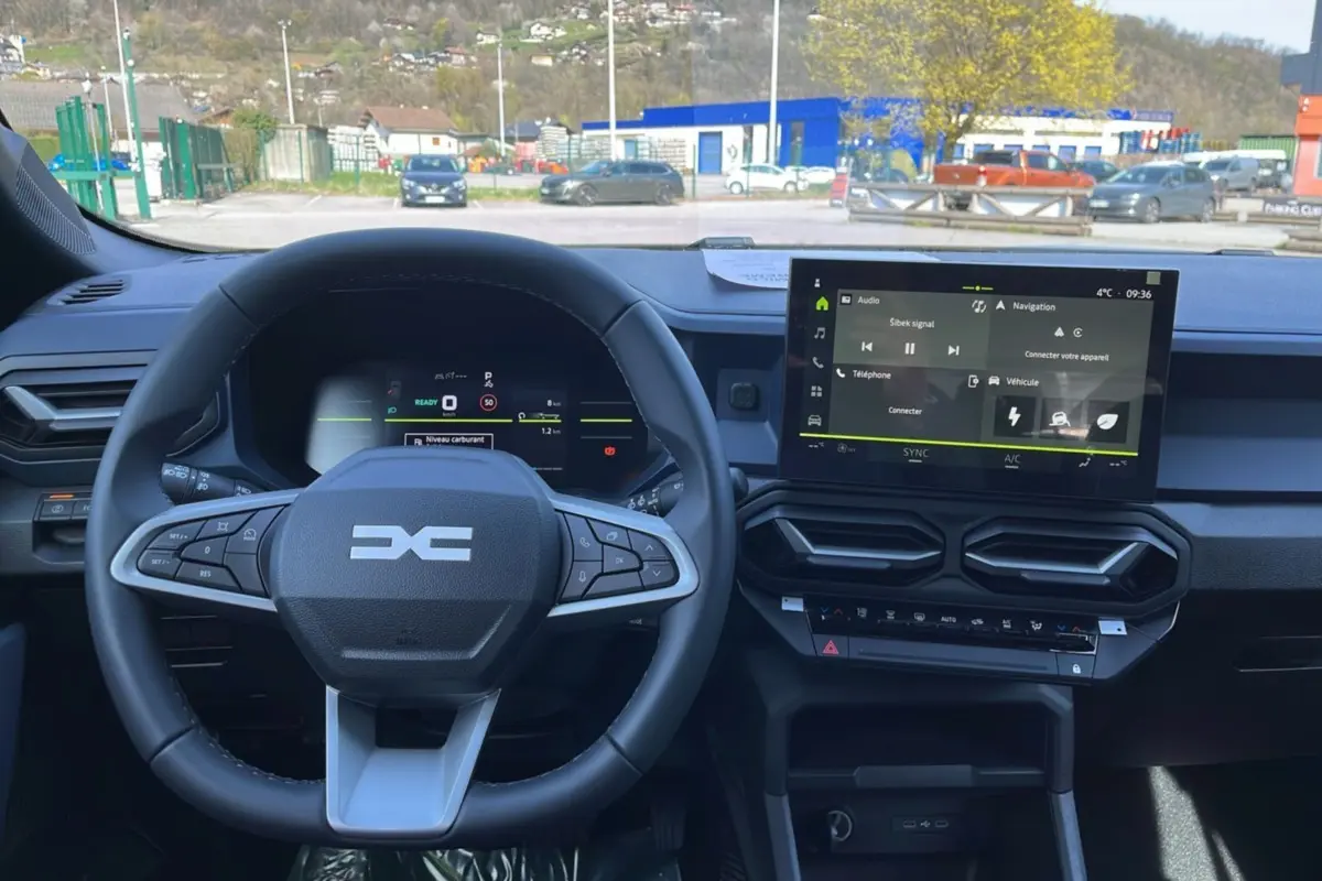 Vue intérieure centrée sur le volant cuir et l'écran tactile 10,1 pouces du tableau de bord du Dacia Bigster gris schiste.