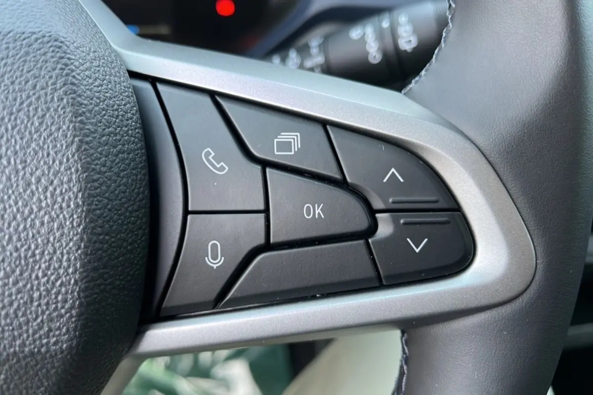 Gros plan sur les commandes multifonctions noires du volant cuir du Dacia Bigster Hybrid 155 Expression Plus, intérieur gris.