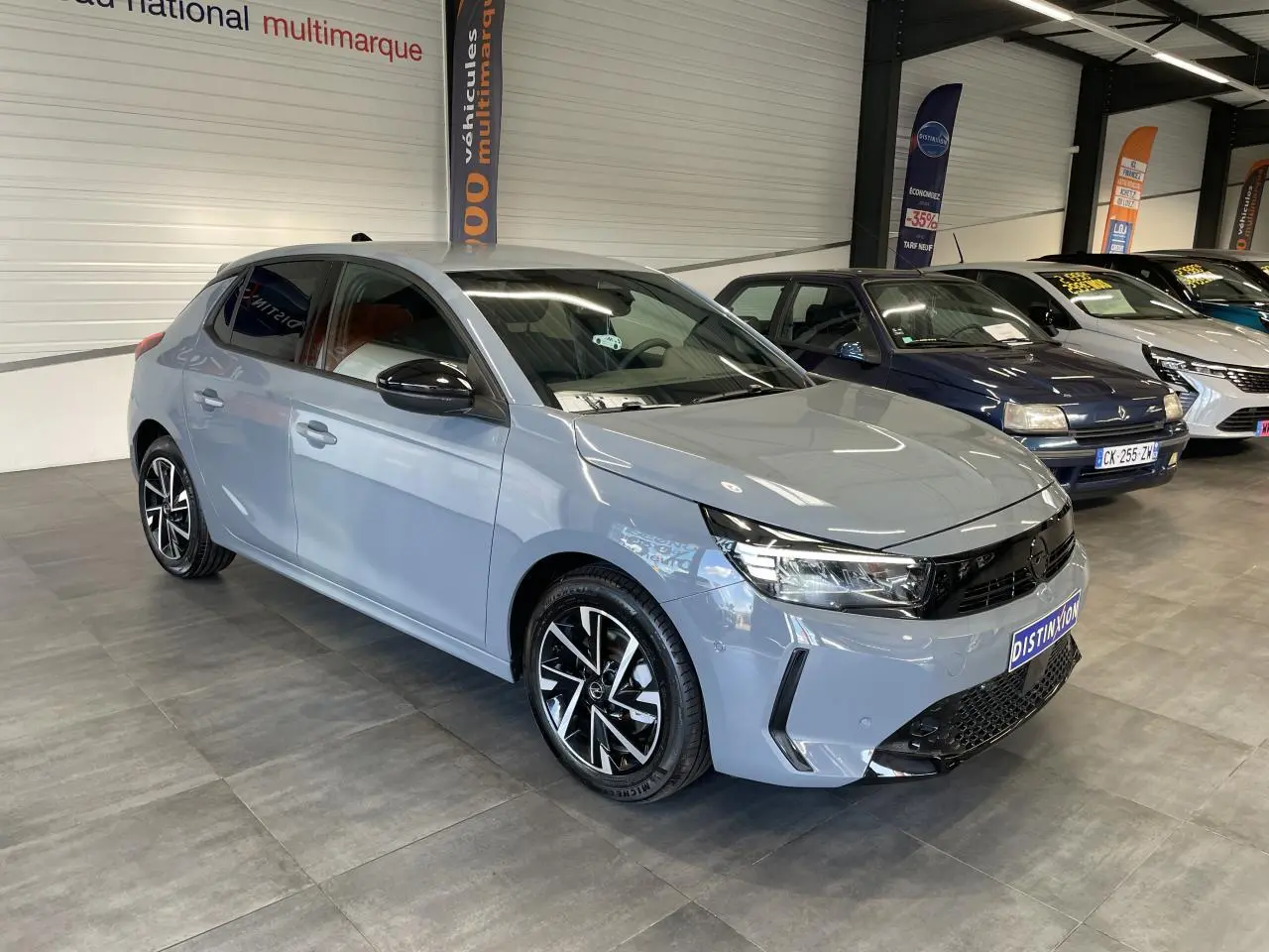 Vue 3/4 avant d'une Opel Corsa gris clair avec jantes alliage noires et vitres arrière surteintées en showroom.