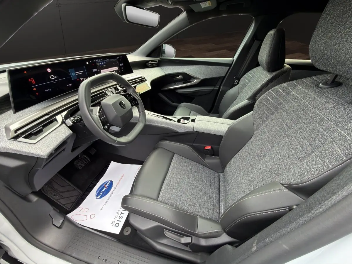 Vue intérieure côté conducteur du Peugeot 3008 2025, montrant le volant cuir multifonctions et les sièges bi-matière gris et noir.