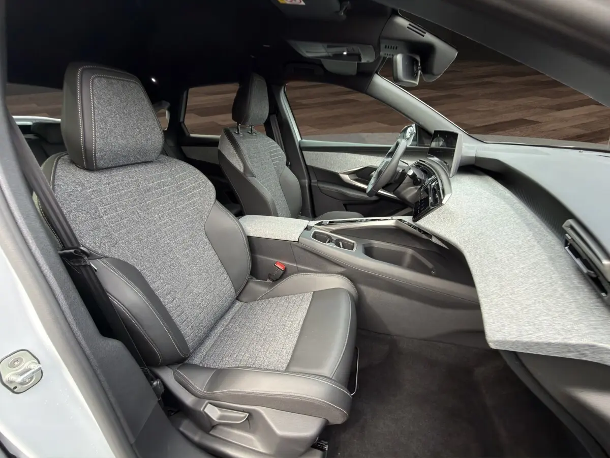 Vue intérieure côté conducteur du Peugeot 3008 blanc 2025, sièges tissu et cuir gris, tableau de bord moderne texturé clair.