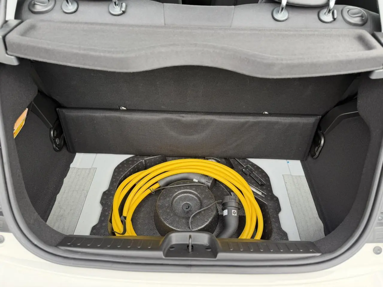 Coffre ouvert d'une Fiat 500 électrique blanc Artic, montrant le câble de recharge jaune rangé sous la trappe.