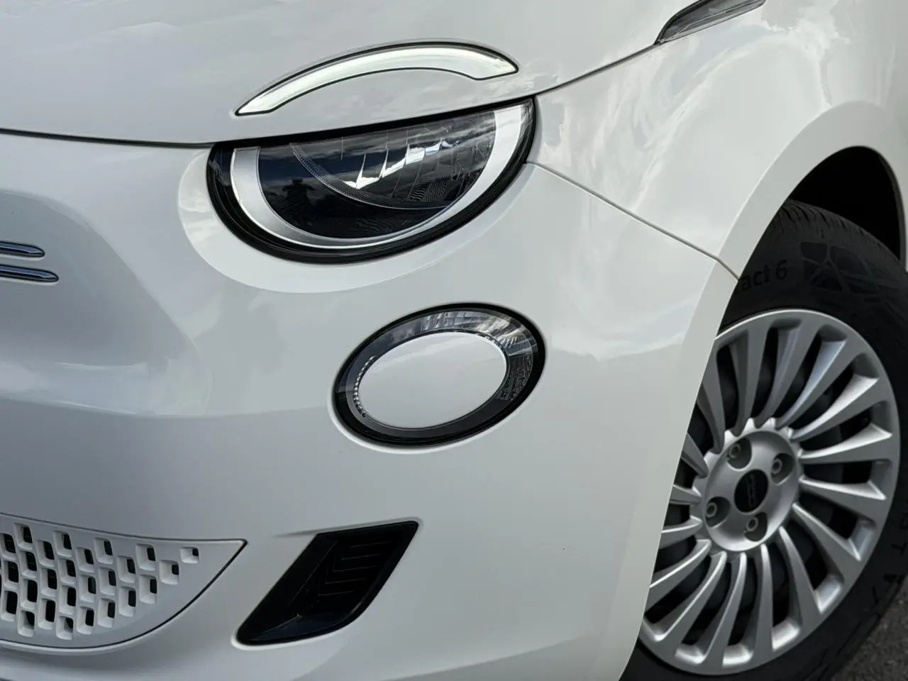 Gros plan sur l'avant droit blanc Artic du FIAT 500 électrique, mettant en valeur le phare LED et la jante alu 16 pouces.