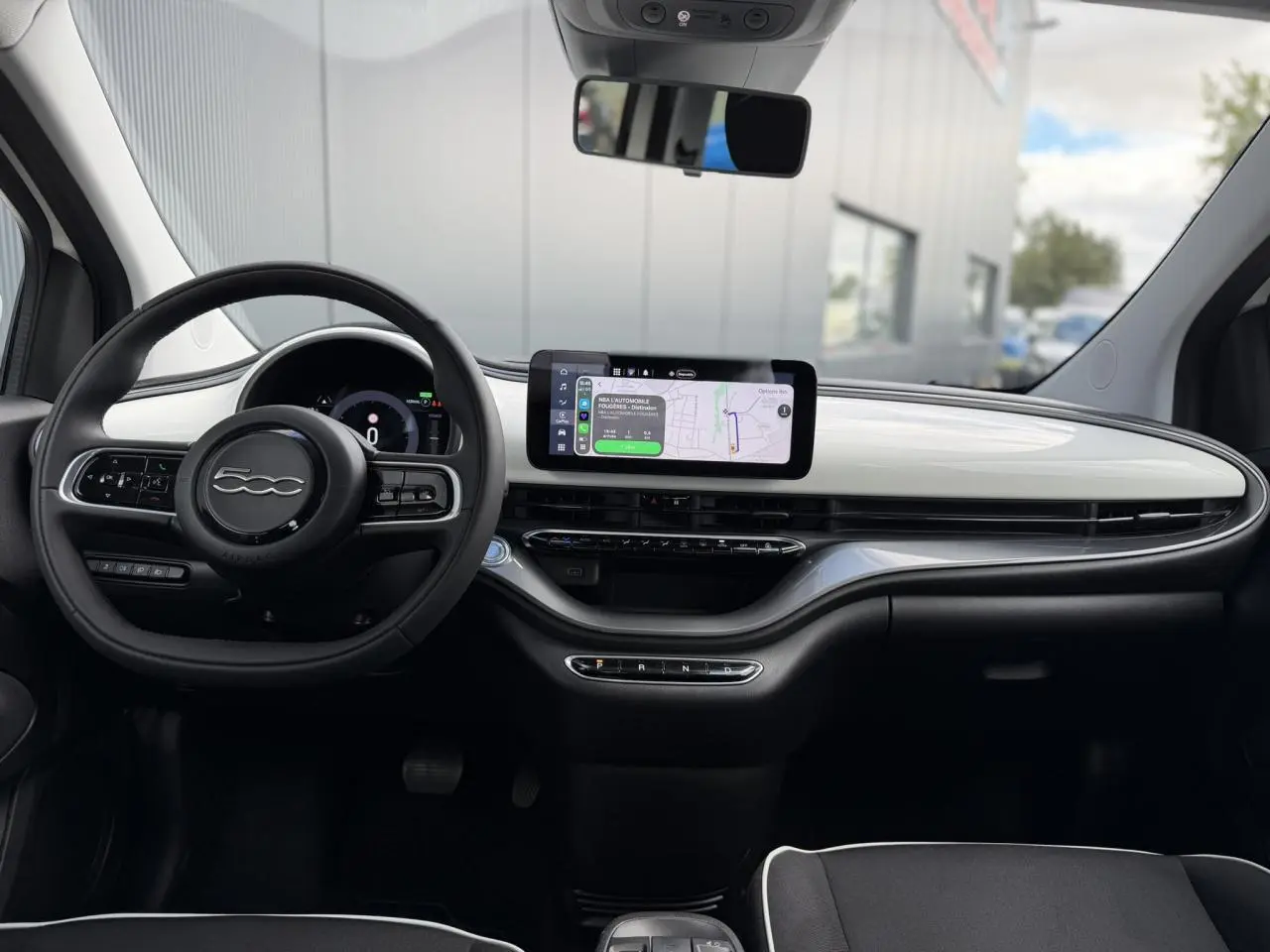 Vue intérieure avant du tableau de bord blanc Artic et volant noir de la Fiat 500 électrique 2024 avec écran tactile central.