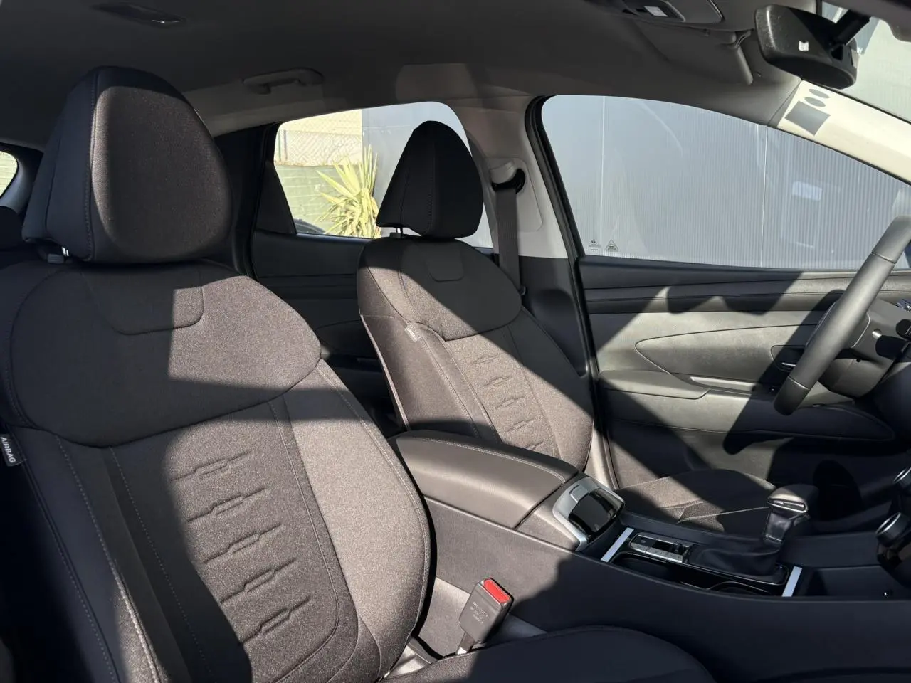 Intérieur du Hyundai Tucson 2025 vu côté droit, sièges tissu gris foncé et console centrale avec levier de vitesses.