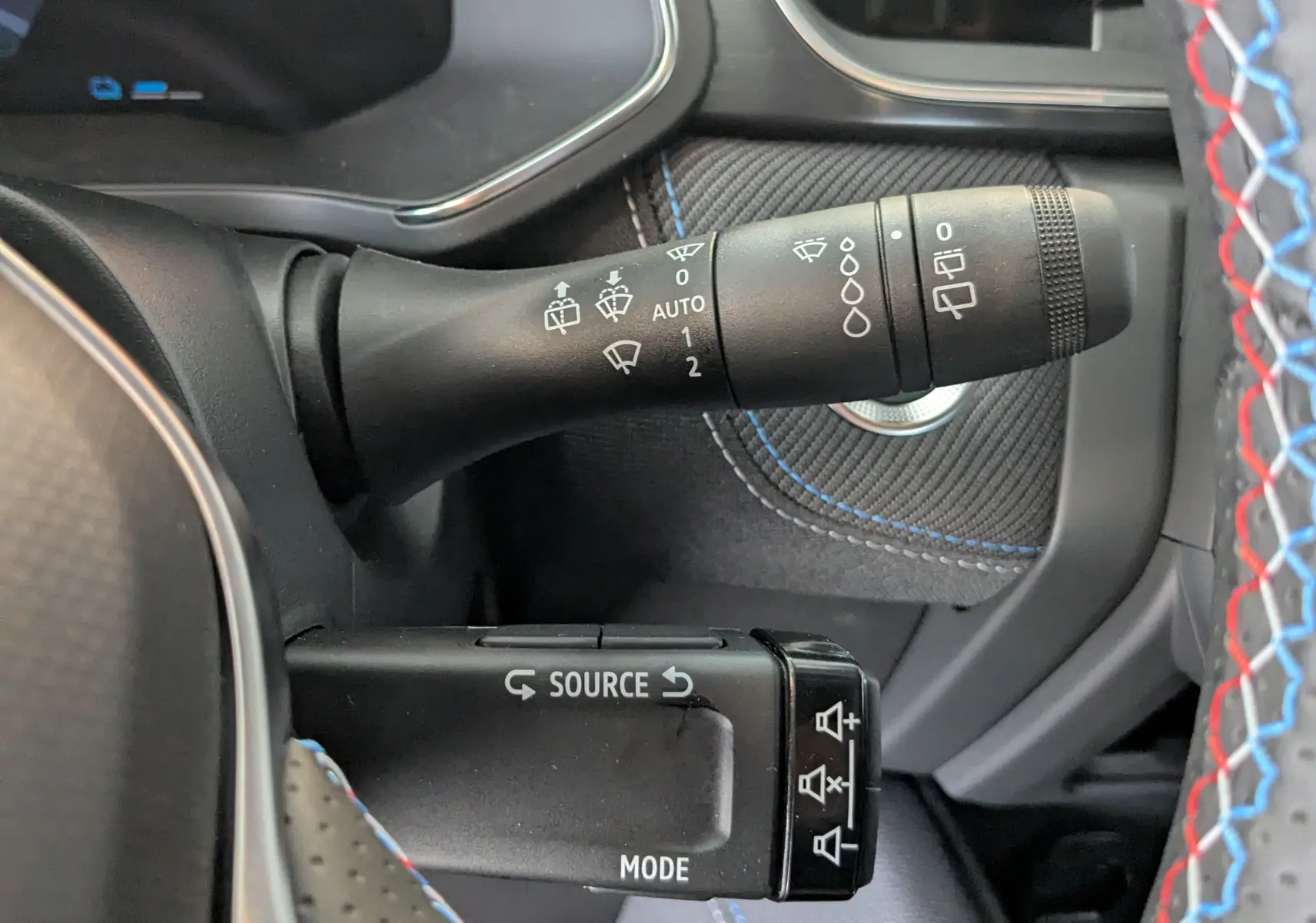 Gros plan sur les commandes de volant du Renault Symbioz bleu iron, avec détails des commandes d'essuie-glace et audio.
