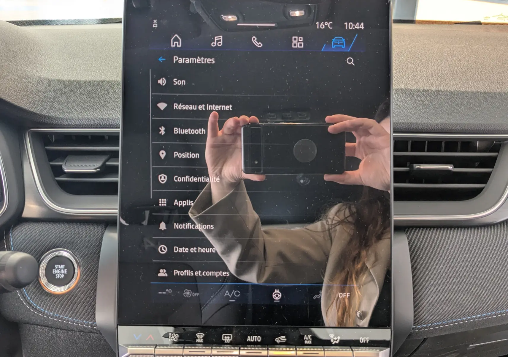 Écran tactile central du tableau de bord du Renault Symbioz bleu Iron, avec menu paramètres affiché et reflet du photographe.