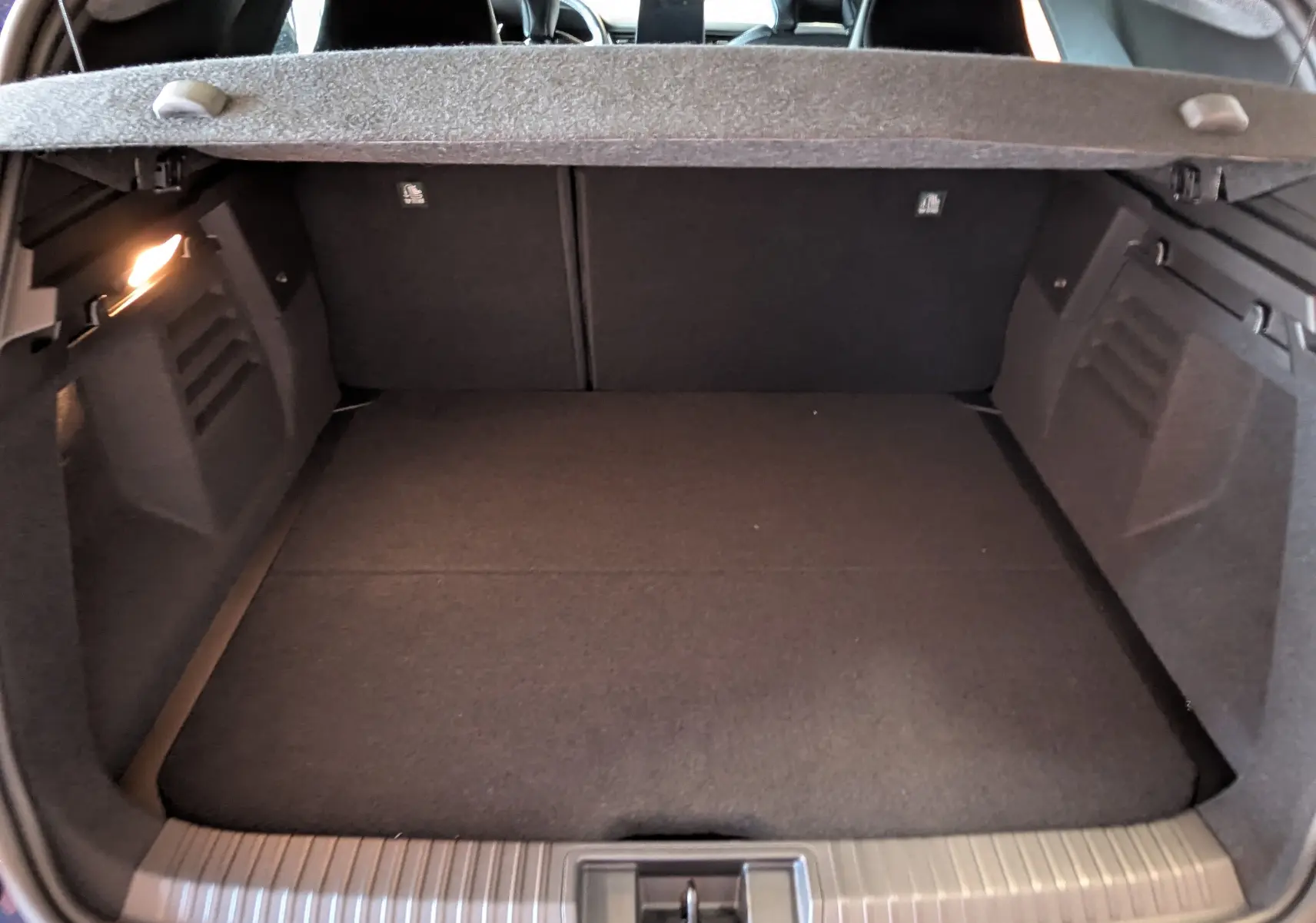 Coffre ouvert vu de l'arrière d'une Renault Symbioz E-Tech hybride, intérieur noir et éclairage latéral allumé.