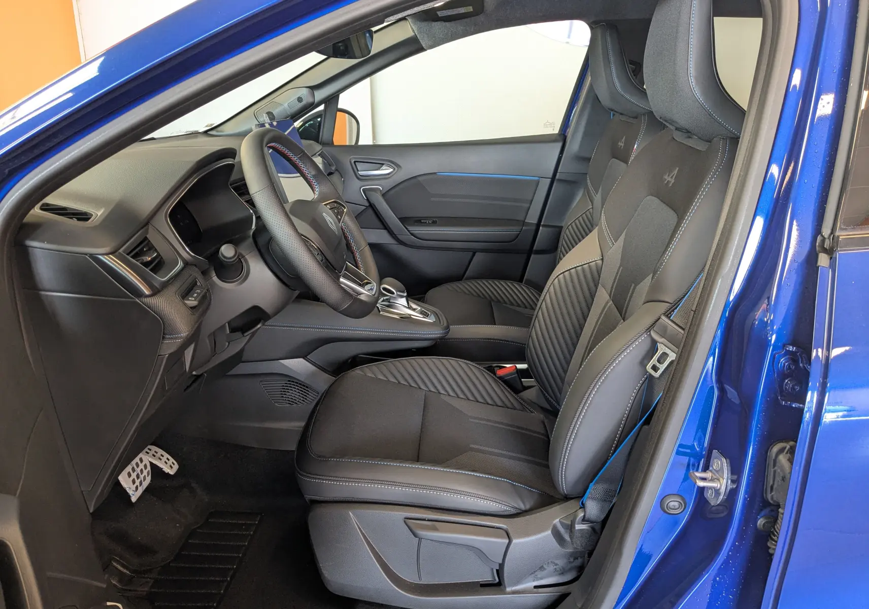 Intérieur côté conducteur du Renault Symbioz bleu iron 2025, sièges noirs avec surpiqûres bleues et volant sport.