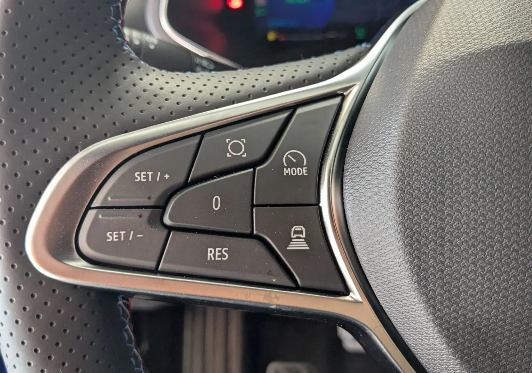Gros plan sur les commandes du volant à gauche de la Renault Symbioz hybride, boutons de régulateur et modes de conduite visibles.
