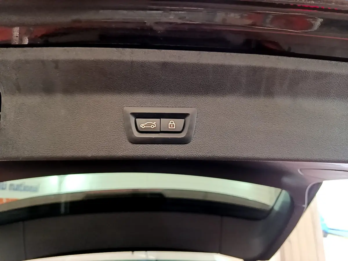 Bouton de fermeture et verrouillage du coffre sur le hayon intérieur d’un BMW X3 noir, vue en contre-plongée.