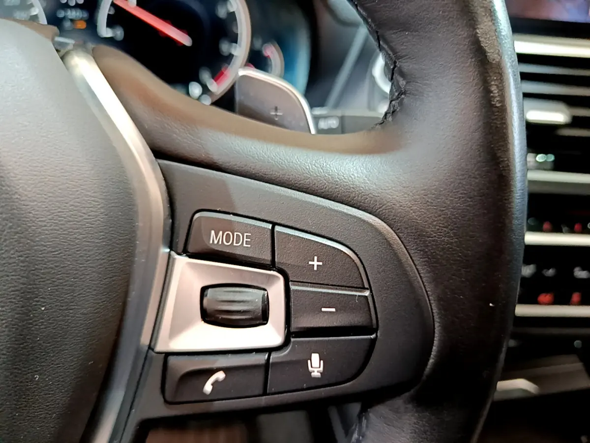 Gros plan sur les commandes du volant en cuir noir d'une BMW X3 2019, boutons mode, volume et téléphone visibles.