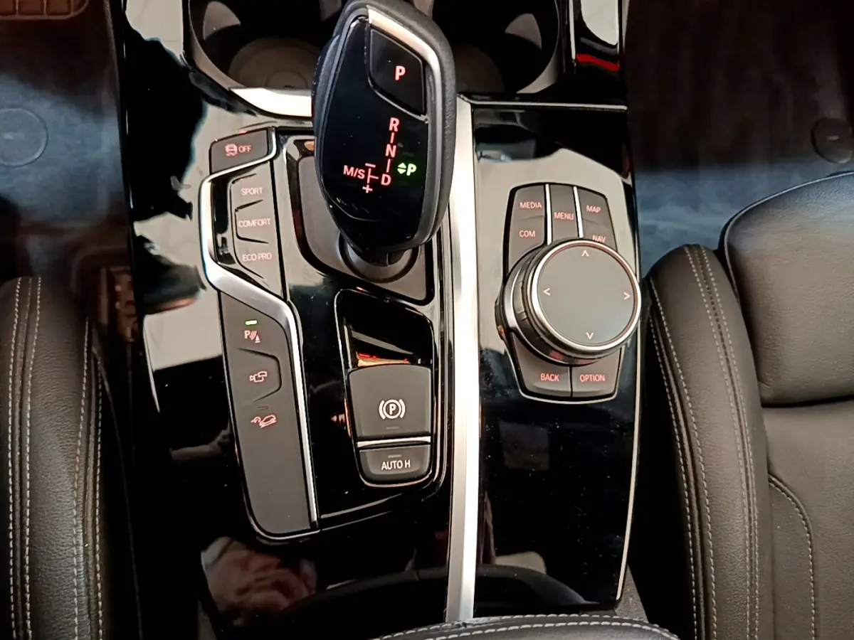 Gros plan sur la console centrale noire brillante du BMW X3 2019 avec levier de vitesse automatique et molette de contrôle.