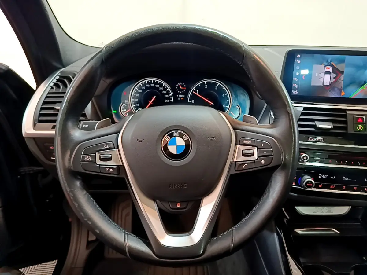 Vue frontale du volant en cuir noir et du tableau de bord digital d'une BMW X3 2019 avec écran tactile et affichage caméra.