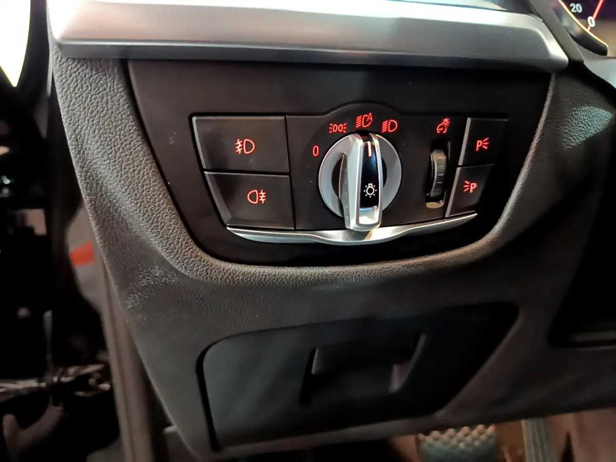 Gros plan sur le panneau de commande des phares avec éclairage rouge dans l'habitacle noir du BMW X3 xDrive20d 2019.