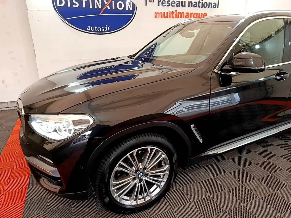 Vue 3/4 avant droit d’un BMW X3 xDrive20d noir brillant, avec jantes alliage et phares LED allumés.