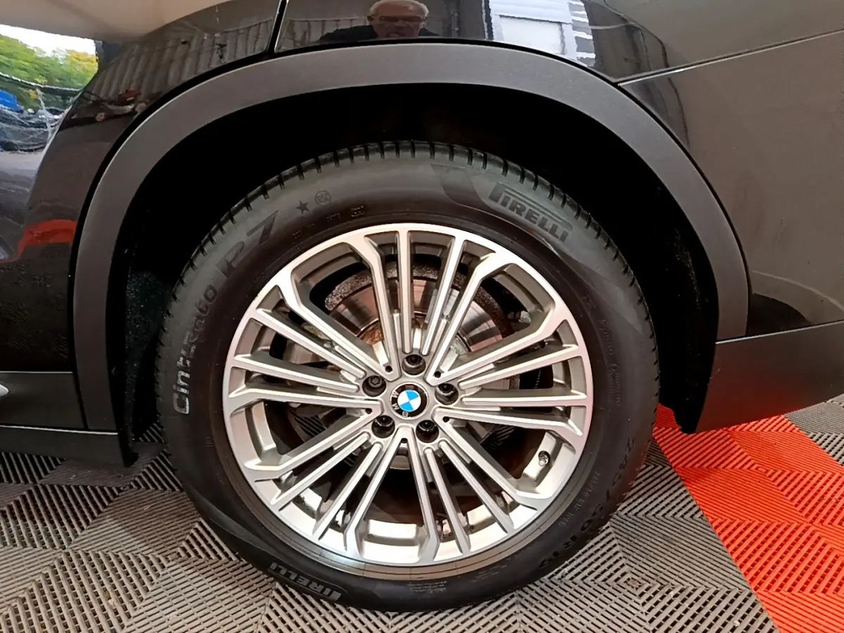 Gros plan sur la roue avant droite d’un BMW X3 noir, jante alliage multi-branches et pneu Pirelli visible.